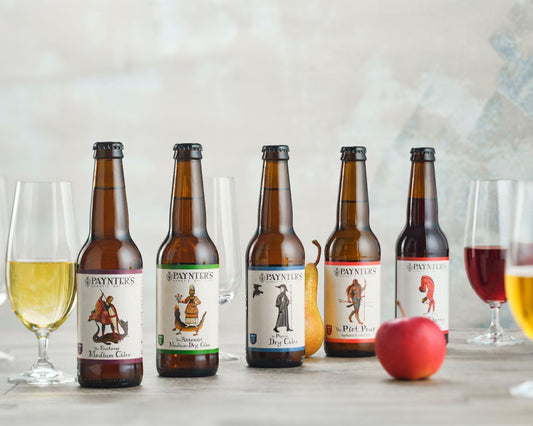 Five bottles of Paynter's beer with their labels displayed on a table with glasses and an apple.