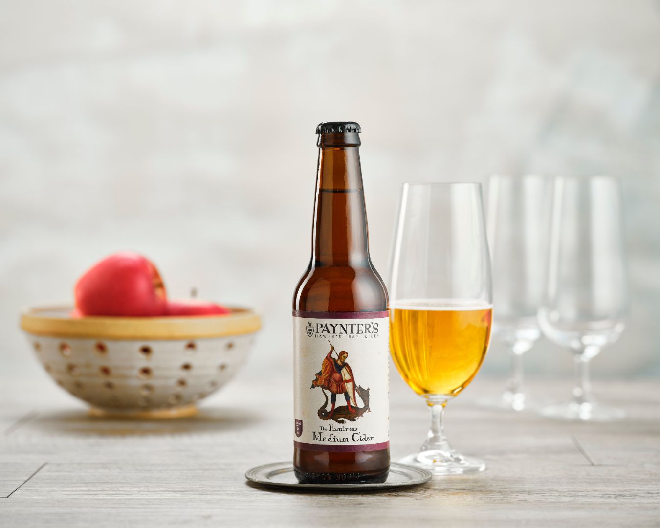 Paynter's cider Huntress bottle with a glass of cider on a wooden surface.